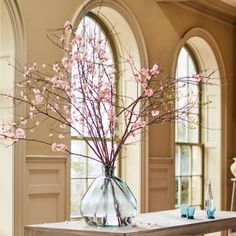 a vase filled with pink flowers sitting on top of a table next to two windows