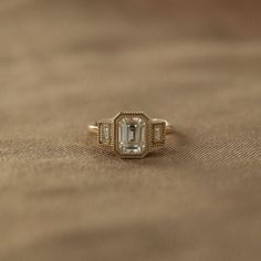 a ring with an emerald colored stone in the center on top of a brown cloth