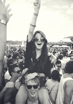 a group of people standing around each other at a music festival with their arms in the air