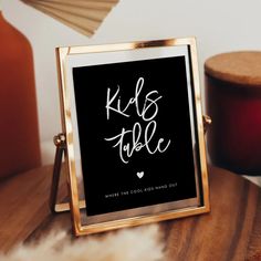 a black and gold frame with the words kids table written in white ink on it