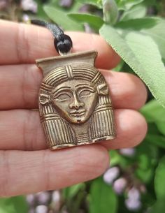 a hand holding a gold colored pendant with an egyptian mask on it's face