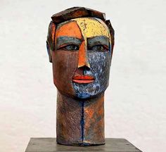 a wooden head with multiple colors on it's face is shown in front of a white wall