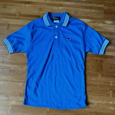 Cross posted and in my vintage booth.  Item may not be available if sold elsewhere. If not available, I will refund you promptly. Thank you for understanding!  Found a collection of cool 80s tennis pieces for boys, girls and women! Featured here is a blue Izod Lacoste striped polo! Was unworn without tags but I washed it because it had been in storage a long time.  Tagged a 14 but fits smaller, see measurements below.  DETAILS: Good Condition 1980s Era 50% Cotton, 50% Polyester Solid blue with white pin stripes Cotton ribbed collar and arm cuffs 2 buttons at neck Straight cut Washed, ready to wear **faint fade line down back from being folded for so long LABEL:  Izod Lacoste Size 14  MEASUREMENTS while flat: Shoulder:  14" Sleeves:  7" Bust:  30" Waist:  28" Hem:  29" Length:  22" MODERN F 80s Tennis, Vintage Booth, Izod Lacoste, Tennis Shirt, Arm Cuffs, White Pin, White Polo Shirt, Tennis Shirts, White Polo