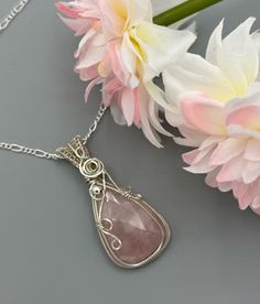 a necklace with a pink stone hanging from it's side next to some flowers