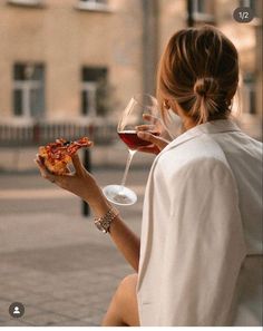 a woman holding a slice of pizza next to a glass of wine