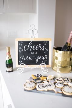 a table topped with cookies and champagne next to a sign that says cheers to a new year