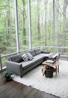 a living room filled with lots of furniture and large glass windows overlooking the woods on a sunny day