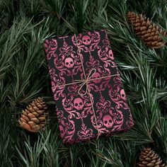 a present wrapped in pink and black paper with skulls on it, surrounded by pine cones