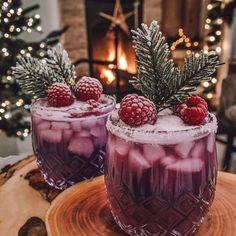 two glasses filled with ice and raspberries sitting on top of a wooden table