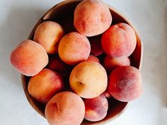 a wooden bowl filled with peaches on top of a white countertop next to a knife