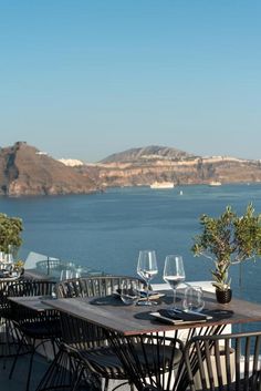 an outdoor dining area overlooking the water and mountains with wine glasses on top of it