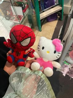 hello kitty and spider - man stuffed animals are being held by someone's hand