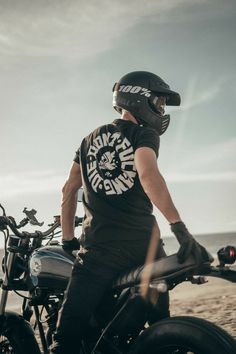 a man standing next to his motorcycle on the beach