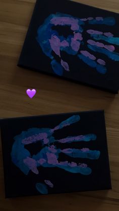 two handprints on black paper with a pink heart in the middle and purple hands