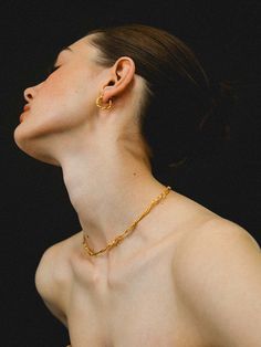 a woman wearing a gold necklace and earring is looking up into the sky with her eyes closed