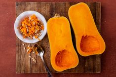 two halves of butternut squash on a cutting board with a spoon next to it