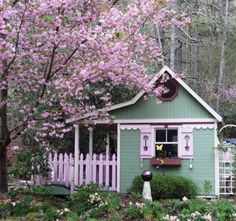 a small green house with pink flowers on the trees