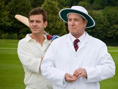 two men standing next to each other in front of a field with trees and grass