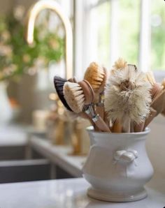 a white vase filled with different types of hairbrushes on top of a counter