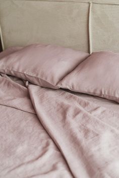 an unmade bed with pink linens and pillows on the headboard is shown