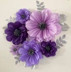 paper flowers are arranged on the wall with leaves and stems in purple, lavender and silver colors