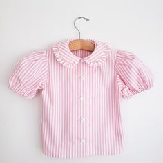 Ruffle Peter Pan collar shirt with puffy sleeves for toddler girls ❤Made to order.  Vintage inspired shirt, perfect for any occasion.  Made of 100% cotton shirting fabric in pink and white stripes. ❤Buttons may vary. ☆☆ Listing is for the shirt only☆☆ ▪︎Matching pieces here▪︎ https://www.etsy.com/shop/CeciliaAndMae?ref=simple-shop-header-name&listing_id=678216147&section_id=26035288 *More shirt options here* https://www.etsy.com/shop/CeciliaAndMae?ref=simple-shop-header-name&listing_id=678216147&section_id=26047885 Turnaround time is 1-3 weeks  Size chart for the blouse as follows: Chest~Waist~Hip 2T 21~20 3T 22~20~20 4T 23~21~24 5T 24~21 1\2~25 6 25~22~26 7 26~23~27 8 27~23 1/2~28 10 28 1/2~24 1/2 12 30~25 1/2~32 Finished length by size 2T~13" 3T~14" 4T~14 3/4" 5~15 1/2" 6~16  7~16 1/2" 8 Ruffle Collar Shirt, Red Suspenders, Peter Pan Collar Shirt, Ruffle Collar Blouse, Shirting Fabric, Polka Dot Shirt, Vintage Inspired Outfits, Pink And White Stripes, Girls Blouse