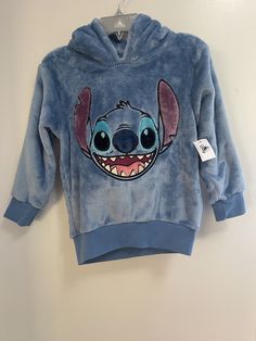 a blue hoodie with stitching on the front and ears is hanging up against a white wall