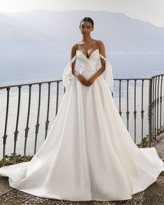 a woman in a white wedding dress standing on a balcony overlooking the water and mountains