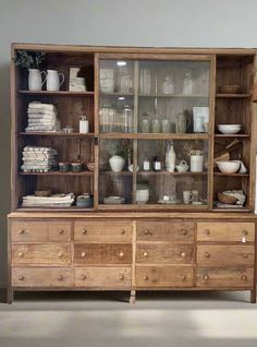 an old wooden cabinet with glass doors and shelves filled with dishes, cups and vases