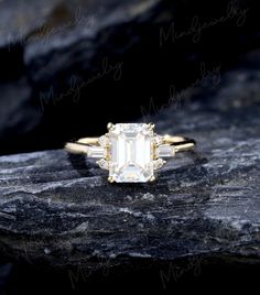 an emerald and diamond ring sitting on top of a rock