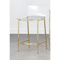 a white and gold bar stool with a glass seat on the bottom, in front of a white wall