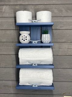 three blue shelves with white towels and two vases on each shelf in front of a wooden wall