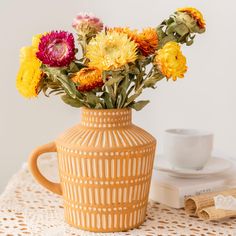 a vase filled with colorful flowers sitting on top of a table next to a cup