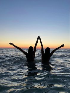 two people are in the water with their arms up and one person is raising their hands