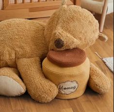 a teddy bear laying on the floor next to a crib with a toy in it's mouth