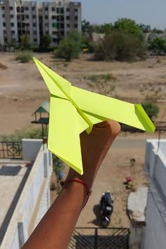 a person holding up a yellow paper airplane