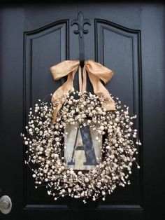 a wreath with the letter a on it is hanging on a black front door, decorated with baby's breath