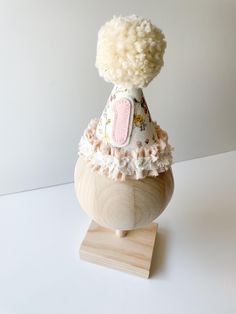 a white stuffed animal sitting on top of a wooden stand with a flowered dress