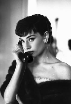 a black and white photo of a woman talking on the phone while wearing a fur coat