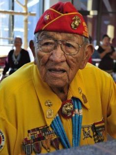 an old man wearing a red hat and yellow shirt sitting at a table with other people