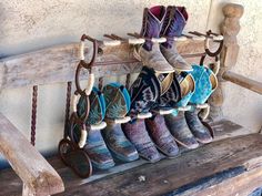 several pairs of cowboy boots are hanging on a wooden bench with rope and hooks attached to it