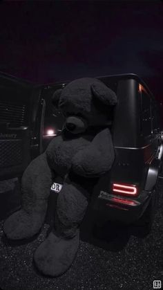 a large black teddy bear sitting in the back of a truck with its lights on