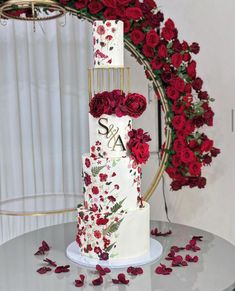 a three tiered wedding cake with red roses around it