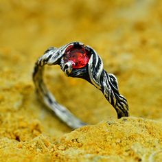 a close up of a ring with a red stone in it on some dirt and yellow sand