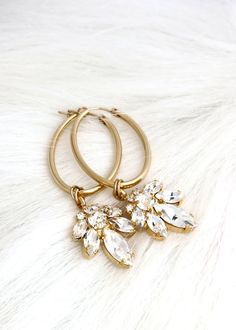 two pairs of gold hoop earrings with clear crystal stones on white fur background, close up