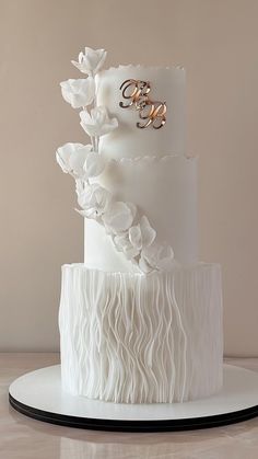 a three tiered white wedding cake with ruffles and gold rings on top