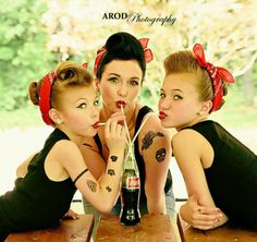 three beautiful young women sitting at a table with a bottle in their hands and one holding a straw up to her mouth