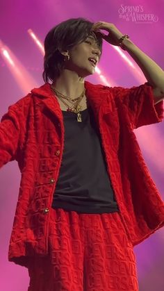 a woman standing on top of a stage holding her hand to her head and wearing a red jacket