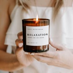 a woman holding a candle that says relaxation on it in front of her face and hands