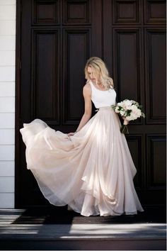 a woman in a white dress is standing by a door and holding a flower bouquet